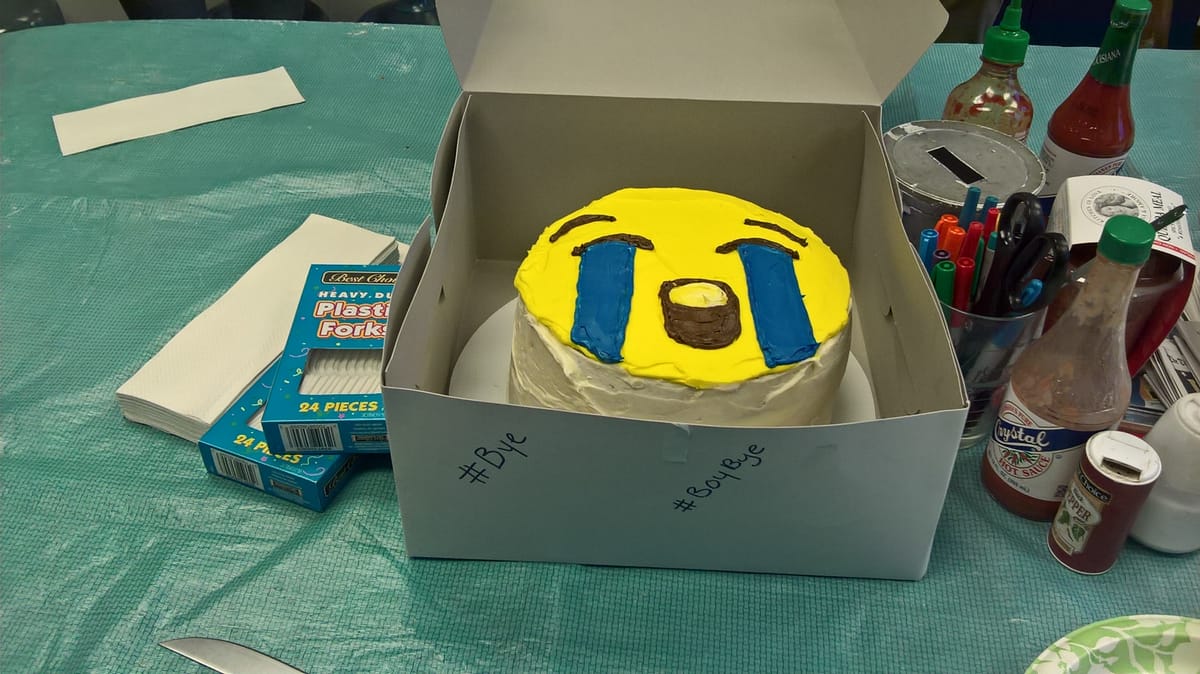 A beautiful cake that looks like the bawling emoji, on a table with plastic forks, crystal sauce, and various other clutter